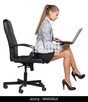 Geschäftsfrau, sitzen auf den Rand der Bürostuhl, mit Laptop auf den Knien. auf den Bildschirm schauen. Auf weissem Hintergrund Stockfoto