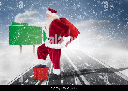 Santa springt mit seinem Beutel gegen Straßen, die über den Wolken mit leeren Wegweiser Stockfoto