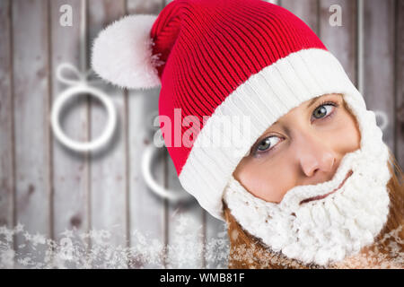 Hübsche Rothaarige in santa Mütze und Bart gegen verwackelte Weihnachtsschmuck auf Holz Stockfoto