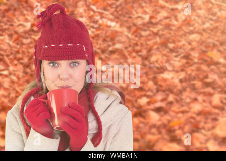 Happy Blondine im Winter Kleidung holding Becher gegen Herbst Blätter auf dem Boden Stockfoto