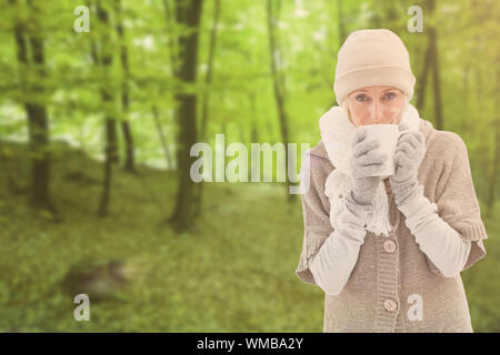 Frau in warme Kleidung holding Becher gegen Bäume in den herbstlichen Wald Stockfoto