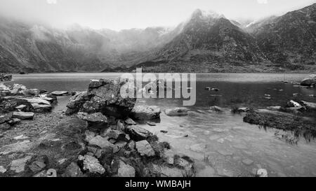 Atemberaubende dramatische Winterlandschaft Bild von Llyn Glyders Idwal und schneebedeckten Bergkette in Snowdonia in Schwarz und Weiß Stockfoto