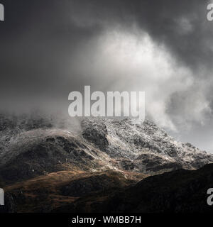 Atemberaubende Moody dramatische Winterlandschaft Bild von schneebedeckten Tryfan Berg in Snowdonia bei stürmischem Wetter Stockfoto