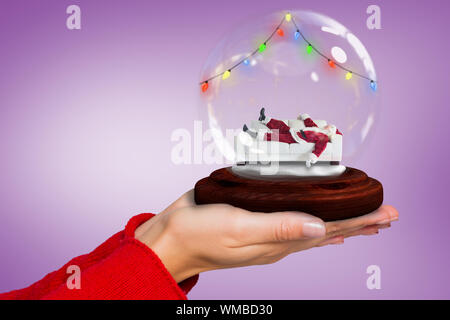 Das zusammengesetzte Bild von Hand santa Snow Globe gegen lila Vignette Stockfoto