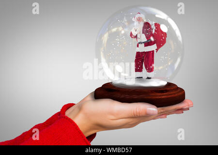 Das zusammengesetzte Bild von Hand santa Snow Globe gegen Grau Vignette Stockfoto