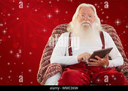 Smiling Santa mit Tablet-PC auf dem Sessel vor rotem Hintergrund Stockfoto