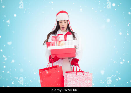 Überrascht brunette im Winter Kleidung halten viele Geschenke und Shopping Taschen gegen den blauen Vignette Stockfoto