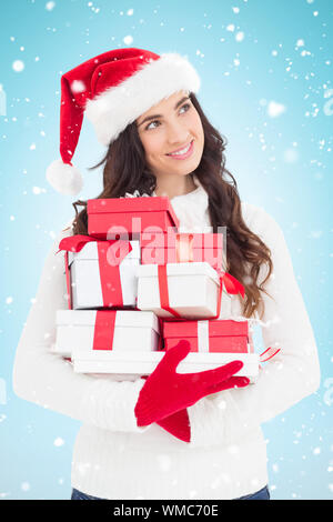 Freudige Brünette in Santa Hat und Red Handschuhe holding Stapel der Geschenke vor blauem Hintergrund mit Vignette Stockfoto