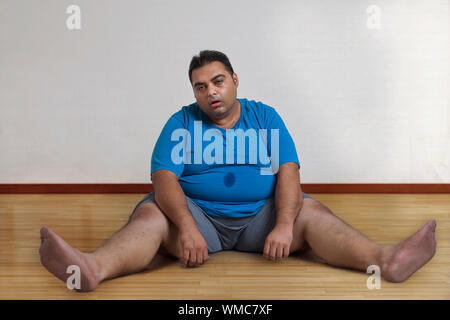 Beleibte Mann sitzt auf dem Boden und die Beine spreizen müde nach dem Training Stockfoto
