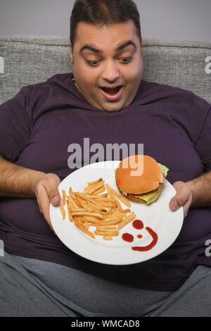 Happy beleibten Mann hält einen Teller mit Burger und Pommes Frites mit einem Smiley aus Tomatensauce Stockfoto