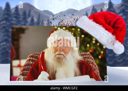 Santa claus Schreiben seine Liste mit einem Federkiel gegen niedlichen Christmas Village unter riesigen Vollmond Stockfoto