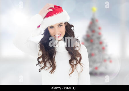 Verwirrt Brünette in Santa Hut gegen blurry Christbaum im Zimmer Stockfoto