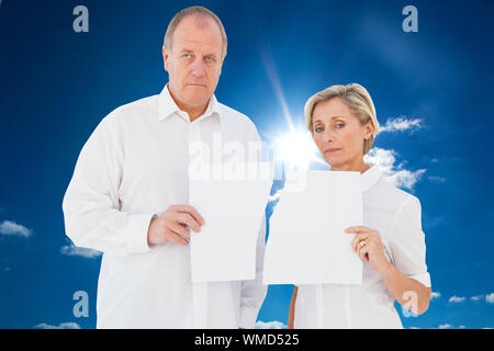 Verärgert Paar hält zerrissenes Stück Papier gegen bewölkten Himmel mit Sonnenschein Stockfoto