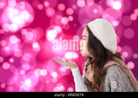 Brunette im Winter Kleidung blasen Küssen gegen Licht leuchtenden Punkte auf Rosa Stockfoto