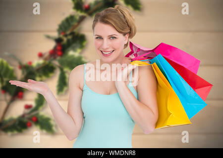 Lächelnde Frau präsentieren, während sie Einkaufstaschen gegen Holly auf Holz verschwommen Stockfoto
