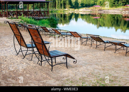 Zone Rest. Holz Sonnenliegen und Stühle mit Tischen stehen am Strand am See, mit Blick auf den See. Weißrussland Stockfoto