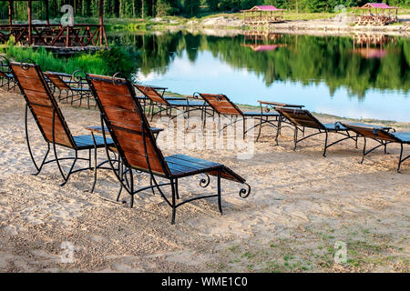 Zone Rest. Holz Sonnenliegen und Stühle mit Tischen stehen am Strand am See, mit Blick auf den See. Weißrussland Stockfoto