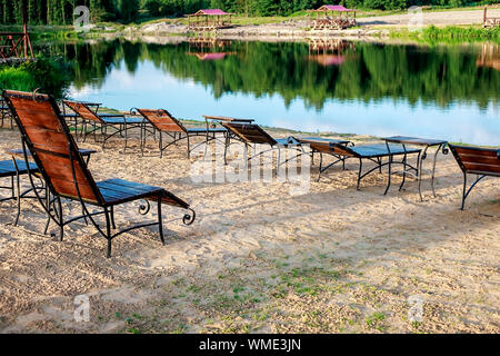 Zone Rest. Holz Sonnenliegen und Stühle mit Tischen stehen am Strand am See, mit Blick auf den See. Weißrussland Stockfoto