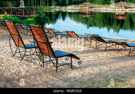 Zone Rest. Holz Sonnenliegen und Stühle mit Tischen stehen am Strand am See, mit Blick auf den See. Weißrussland Stockfoto