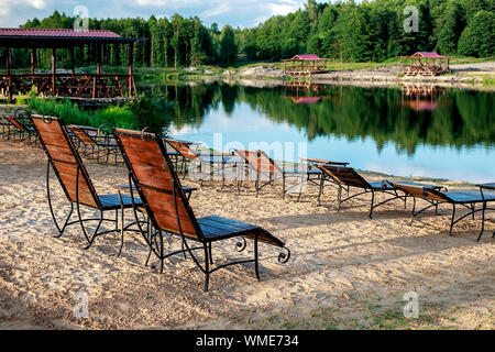 Zone Rest. Holz Sonnenliegen und Stühle mit Tischen stehen am Strand am See, mit Blick auf den See. Weißrussland Stockfoto