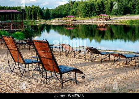 Zone Rest. Holz Sonnenliegen und Stühle mit Tischen stehen am Strand am See, mit Blick auf den See. Weißrussland Stockfoto