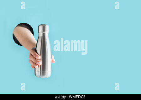 Wiederverwendbare metall Flasche für Getränke in weiblicher Hand durch das Loch im Papier. Individuelle Nutzung. Speichern Sie die Planeten. Null Abfall Konzept. Kunststoff frei. Stockfoto
