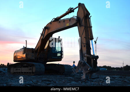 Große Raupenbagger mit hydraulischer Schere auf einer Baustelle vor dem Hintergrund der fantastischen Sonnenuntergang. Road Repair, Asphalt ersetzt werden. S Stockfoto