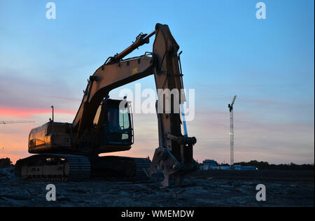 Große Raupenbagger mit hydraulischer Schere auf einer Baustelle vor dem Hintergrund der fantastischen Sonnenuntergang. Road Repair, Asphalt ersetzt werden. S Stockfoto