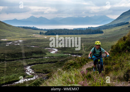 Eine Frau fährt im Sommer auf einem Wanderweg auf der Applecross-Halbinsel im Nordwesten der schottischen Highlands mit einem Mountainbike-Rad. Stockfoto