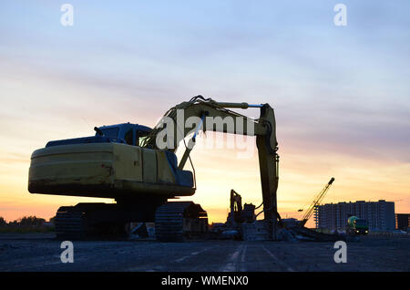 Große Raupenbagger mit mit hydraulischer Hammer bricht Asphalt auf einer Baustelle auf dem Hintergrund Sonnenuntergang. Road Repair, Asphalt replac Stockfoto
