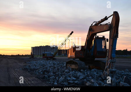 Große Raupenbagger mit hydraulischer Schere auf einer Baustelle vor dem Hintergrund der fantastischen Sonnenuntergang. Road Repair, Asphalt ersetzt werden. S Stockfoto