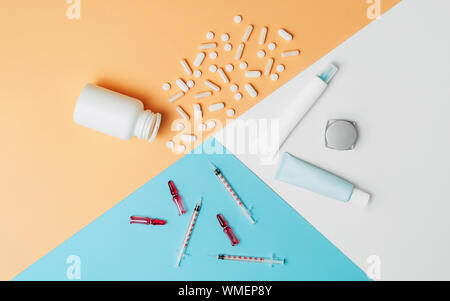 Mock-up kosmetische Tuben, Flaschen mit dem verschütteten Tabletten und Spritzen mit Ampullen auf weiß, orange und blau hinterlegt. Kosmetologie vs Medizin Konzept. F Stockfoto