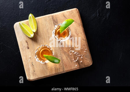 Golden tequila Schüsse mit Salz und Limette, Scheiben, geschossen von oben auf einem schwarzen Hintergrund mit Kopie Raum Stockfoto