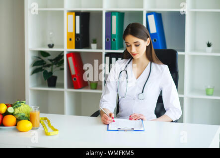 Gesundheit und Schönheit. Der Arzt Zeichen einen Diätplan. Die Ernährungsberaterin hält in den Händen von frischem Obst und Gemüse. Junger Arzt mit einer schönen Stockfoto