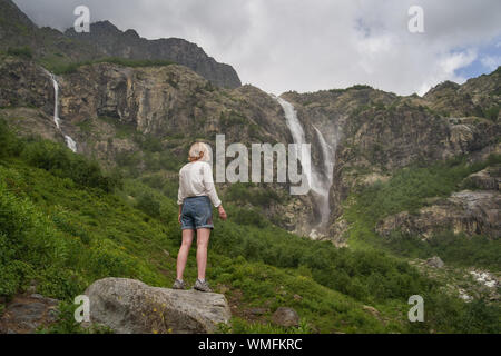Frau, die auf dem Felsen und genießen den Blick auf epische Wasserfall Stockfoto