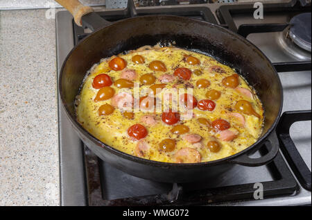 Pfanne voller Omelette mit Cherry Tomaten und Wurstscheiben, stehend auf einem Herd Stockfoto