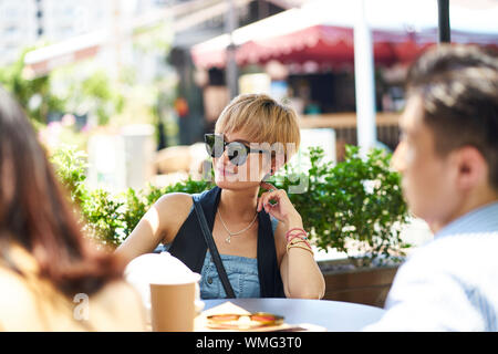 Junge asiatische Frau lächelnd, während im Gespräch mit Freunden im Freien Kaffee shop Stockfoto