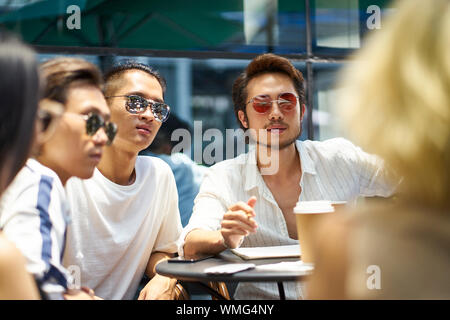 Junge asiatische Studenten in eine Diskussion in der Gruppe an einer im Coffee Shop Stockfoto