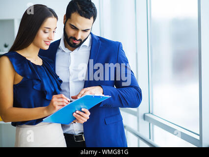 Ziemlich gemischten Rasse Frau und ihren bärtigen mit Phone Kollege um gemeinsames Projekt in Office Unternehmen zu besprechen Stockfoto
