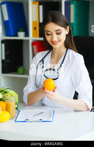 Gesundheit. Arzt Dietologist hält an der frischen Orange Hände. Gesunde Ernährung. Frisches Obst und Gemüse auf den Tisch. Gerne Arzt im Licht Stockfoto