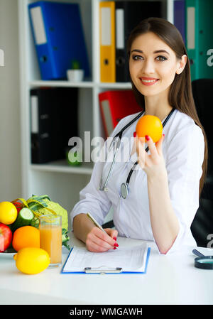 Gesundheit. Arzt Dietologist hält an der frischen Orange Hände. Gesunde Ernährung. Frisches Obst und Gemüse auf den Tisch. Gerne Arzt im Licht Stockfoto