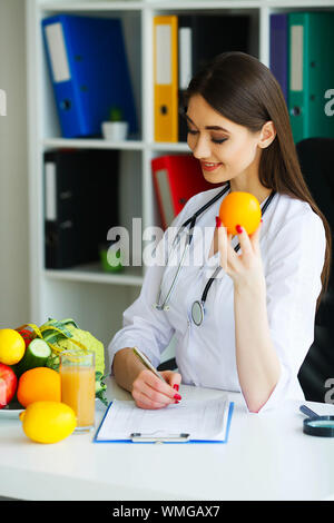 Gesundheit. Arzt Dietologist hält an der frischen Orange Hände. Gesunde Ernährung. Frisches Obst und Gemüse auf den Tisch. Gerne Arzt im Licht Stockfoto