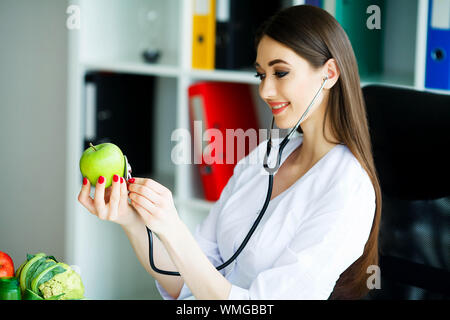 Gesundheit. Das gesunde Essen. Die Ernährungsberaterin hält in den Händen von frischen, grünen Apfel. Frisches Obst und Gemüse auf den Tisch. Gerne Arzt. Hohe Stockfoto