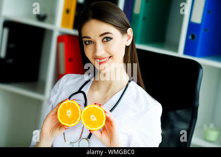 Gesundheit. Arzt Dietologist hält an der frischen Orange Hände. Gesunde Ernährung. Frisches Obst und Gemüse auf den Tisch. Gerne Arzt im Licht Stockfoto