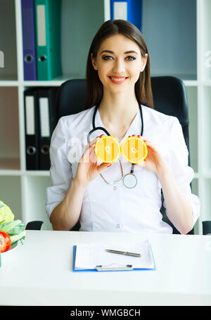 Gesundheit. Arzt Dietologist hält an der frischen Orange Hände. Gesunde Ernährung. Frisches Obst und Gemüse auf den Tisch. Gerne Arzt im Licht Stockfoto