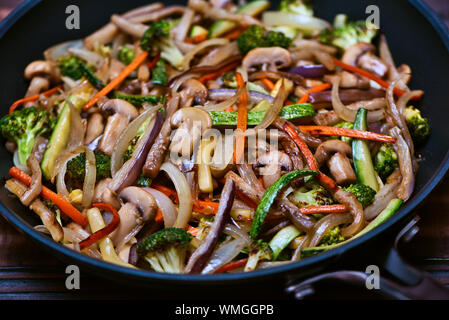 In Juliana Sauted gehacktes Gemüse: Zucchini, Zwiebeln, Auberginen, Möhren, Champignons und Brokkoli in einer Pfanne über einen Vintage Holz- Oberfläche Stockfoto