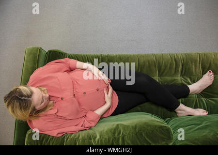 Eine prgnant Frau entspannend auf grünem Sofa ihr Baby bump Holding Stockfoto