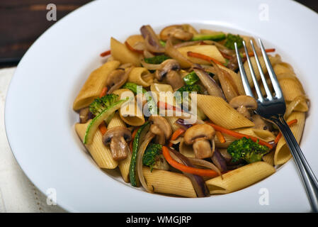 Warme Speise der Penne Rigate Nudeln mit Gemüse in Sauted Juliana: Zucchini, Zwiebeln, Auberginen, Möhren, Champignons und Brokkoli in eine weiße Pasta Platten Stockfoto