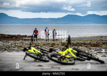 Zwei Männer und eine Frau verlassen Ihre Mountainbikes für einen Spaziergang auf Camasunary Strand auf der Isle of Skye im Sommer. Stockfoto