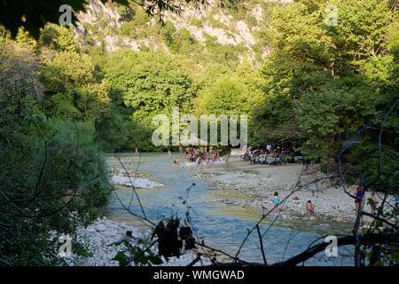 Kinder spielen am Ufer des Acheron Flusses in Acheron Quellen in Griechenland im Sommer in der Nähe eines Restaurants am Wasser mit Familien. Stockfoto